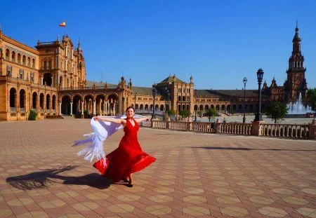 Flamenco dancer in a red dress and a white Spanish shawl dancing in the Plaza de Espana during the Feria de Abril (April fair) in Seville, Spain