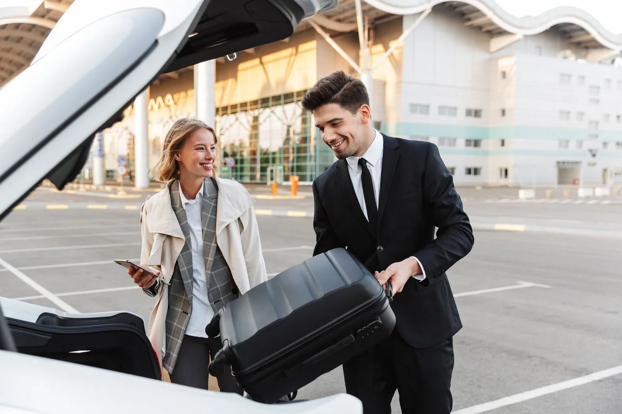 Image of young caucasian businesslike man and woman in formal wear putting travel luggage in car trunk outdoors