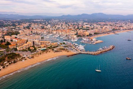 Picturesque aerial view of coastal area of Frejus overlooking marina with moored pleasure yachts and residential districts along waterfront in warm autumn day, France