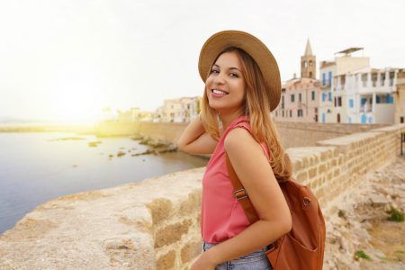 Portrait of smiling relaxed traveler woman walking along Alghero seafront, Sardinia, Italy