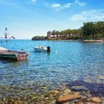 Santa Margherita di Pula (Sardinia) – Cala d’Ostia, crystal clear sea on the bay with a fishing boat.