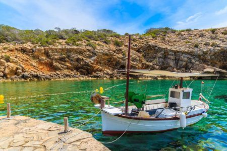 White typical fishing boat anchoring in beautiful Cala Carbo bay with emerald green sea water, Ibiza island, Spain