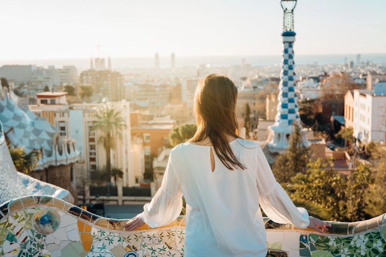 Young female tourist spending vacation in Barcelona,Catalonia,Spain.Traveling to Europe,visiting Parc Guell UNESCO site famous historical landmarks.Panoramic view on entrance.Best sunrise in Barcelona