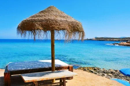 detail of a relaxing area in a Cala Conta beach in Ibiza Island, Spain, with a comfortable sunlounger and a rustic umbrella made of natural fibers