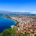 City buildings with red roofs at the shore of a lake with mountains in the background. View of Pogradec city and Ohrid lake, Pogradec, Albania.