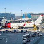 Loading airplane parked by Copenhagen airport building, stairs and luggage carriers nearby