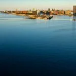 Morning in Copenhagen from the cruise ship terminal, with a view of the city on the horizon, the opera house, spires and domes of several landmarks prominent, in tones of blue, orange and tan