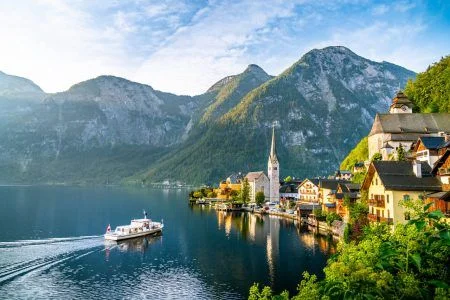 Panorama view of famous old town Hallstatt and alpine deep blue lake with tourist ship in scenic golden morning light on a beautiful sunny day at sunrise in summer, Salzkammergut, Austria