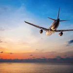 Plane flying over the tropical sea at sunset