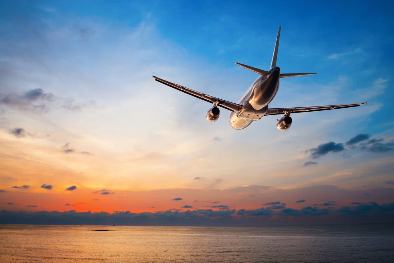 Plane flying over the tropical sea at sunset