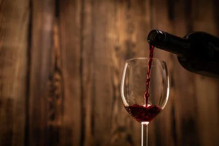 Pouring red wine into the glass against wooden blurred background.