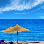 Summer morning pebbly beach with sunbeds and strawy sunshades (Borsh, Albania). Blue sky with some clouds.