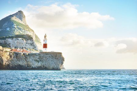 Trinity lighthouse at the rocky shore (cliffs) of the Europa Point. British Overseas Territory of Gibraltar, Mediterranean sea. Epic cloudscape. National landmark, sightseeing, travel destination