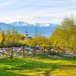 Bansko, Bulgaria spring landscape with the wooden fence, trees, tower of chalet and snowy Rila mountains peaks