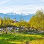 Bansko, Bulgaria spring landscape with the wooden fence, trees, tower of chalet and snowy Rila mountains peaks