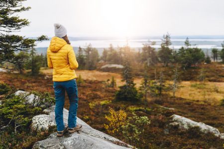 Female traveler in a yellow jacket hiking back in an autumn forest in Finland Lapland. Hiking and adventure.