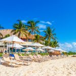 Palm trees parasols umbrellas and sun loungers at the reef coco beach resort on tropical mexican beach in Playa del Carmen Mexico.
