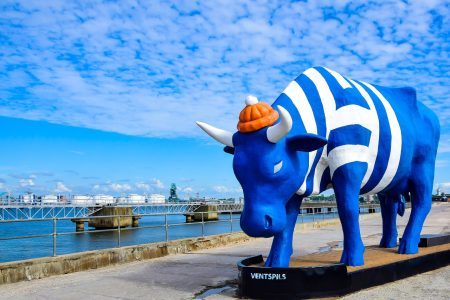Installation a figure of a blue bull in a sailor costume stands on a jetty near the sea in Ventspils, Latvia against the backdrop of the port.